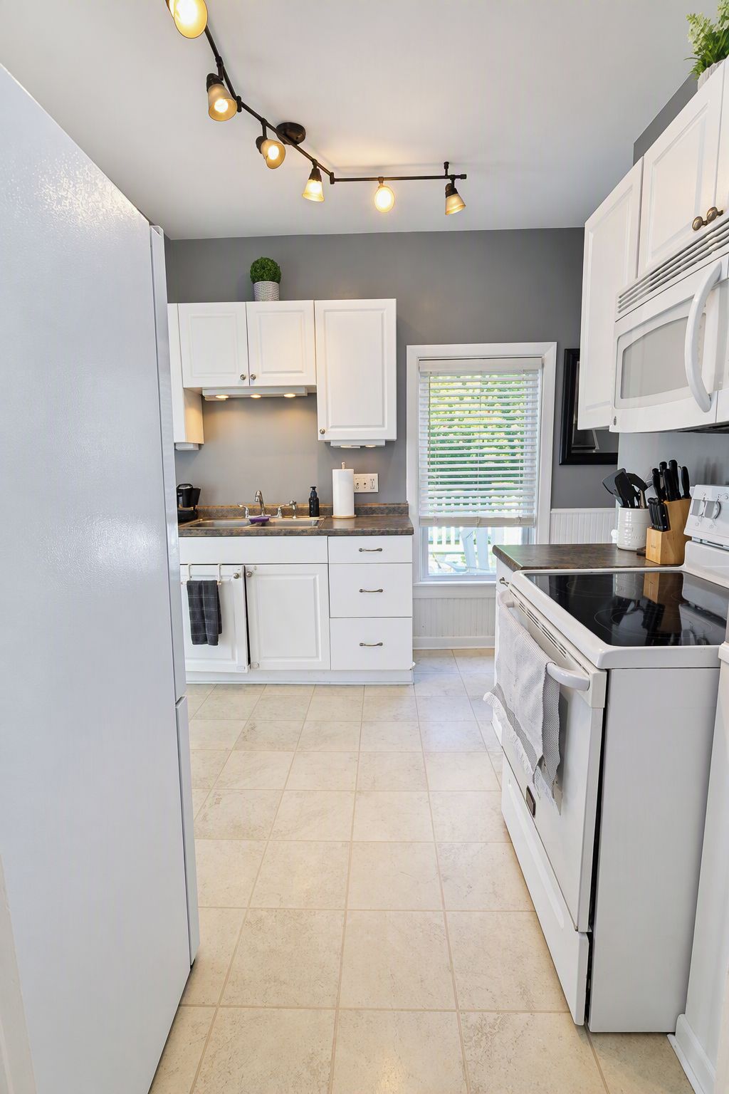 A kitchen with white cabinets, a stove, a microwave, and a window with blinds.