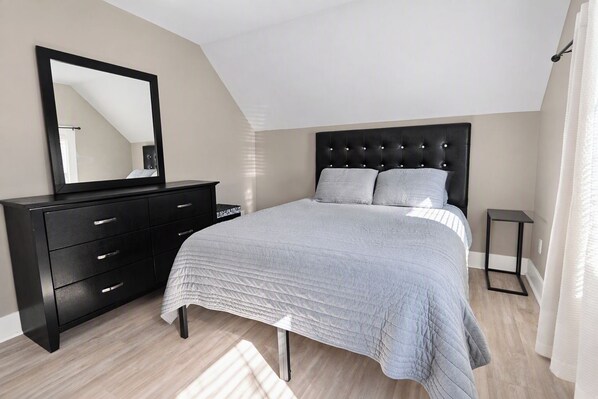 Un dormitorio con cama, cómoda, espejo y una mesita.