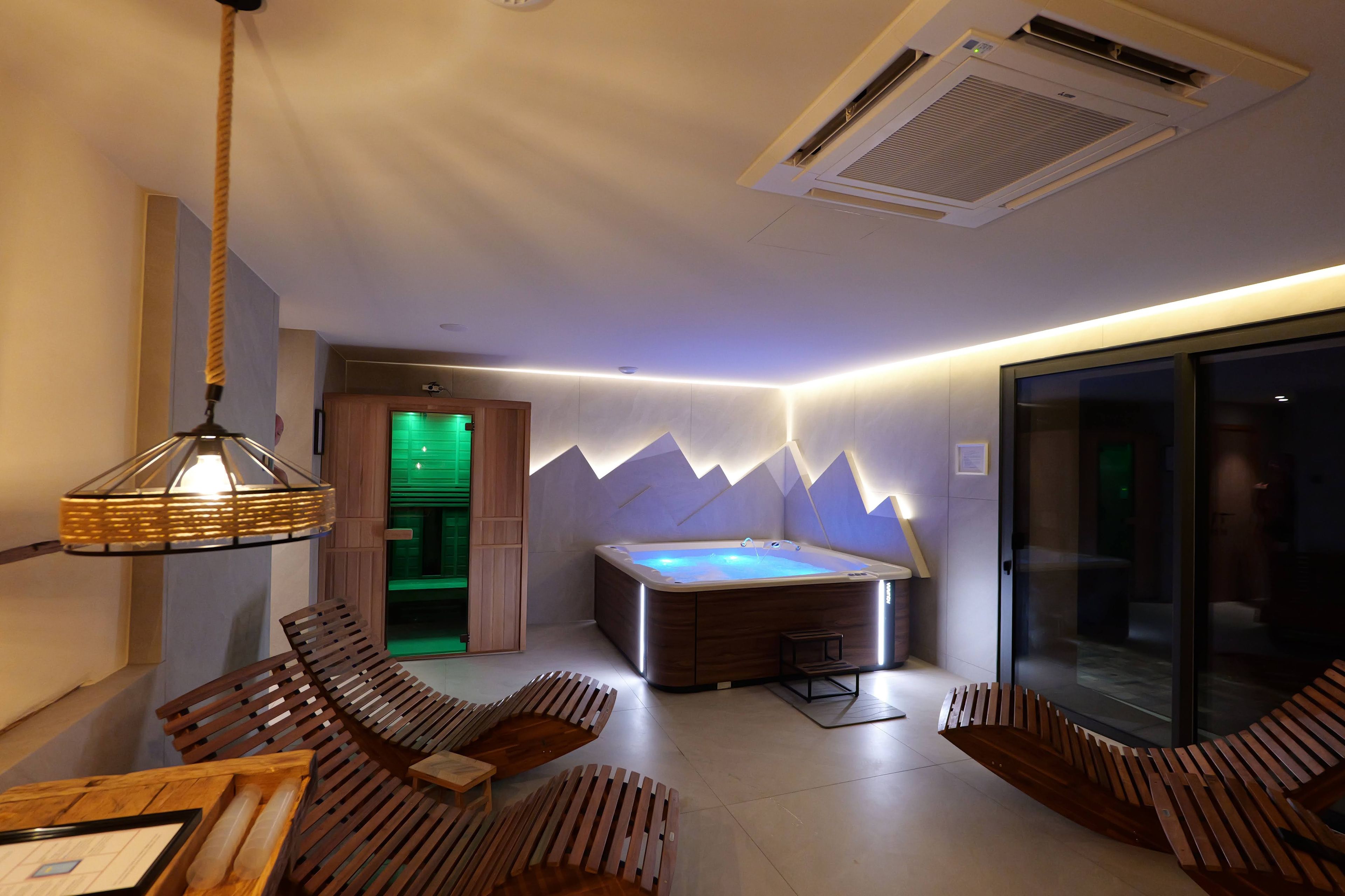 Une salle de spa moderne dotée d’un jacuzzi, de sièges en bois et d’une paroi en verre.