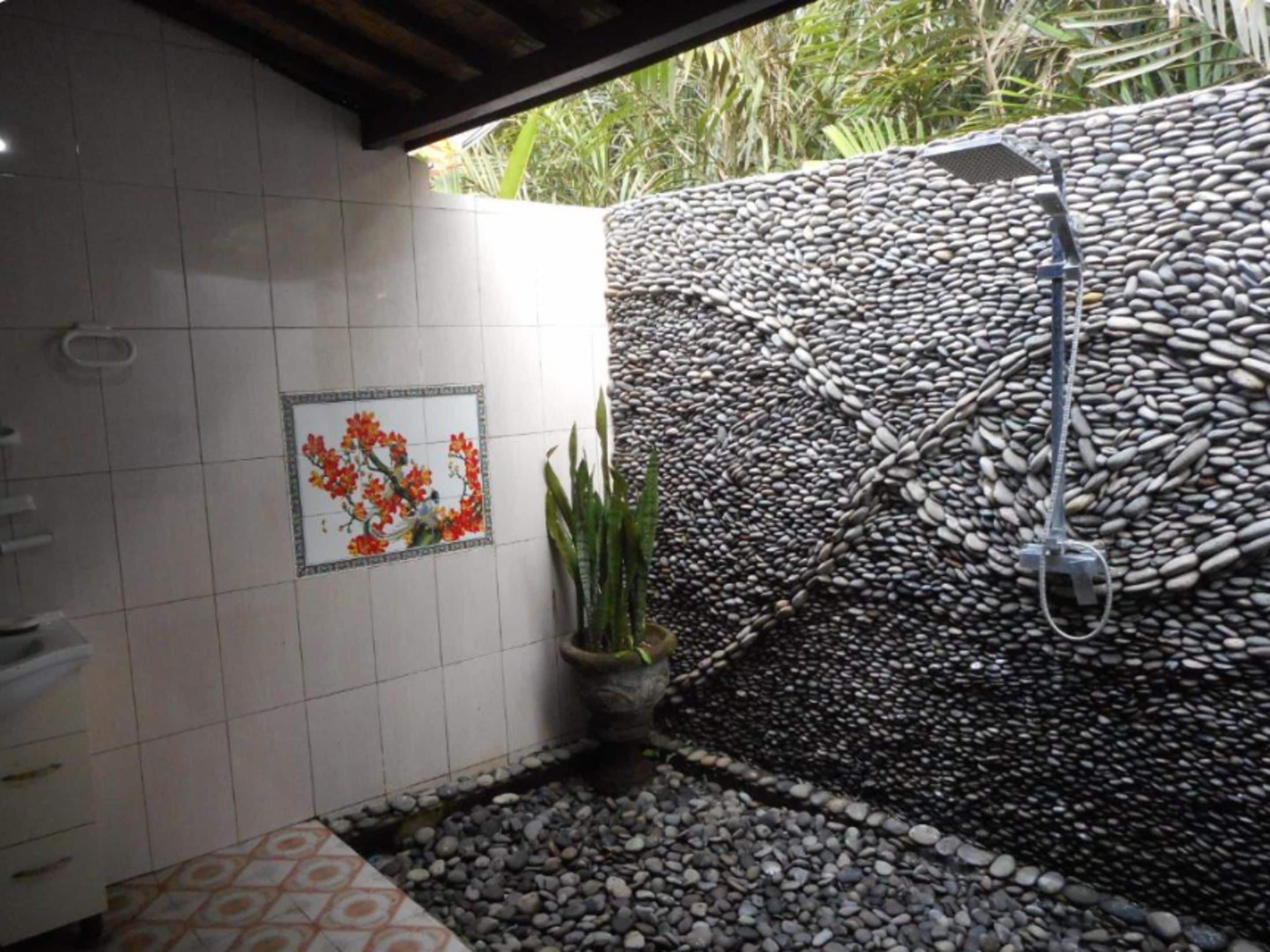 Un baño con pared de azulejos, una ducha y una planta en maceta.