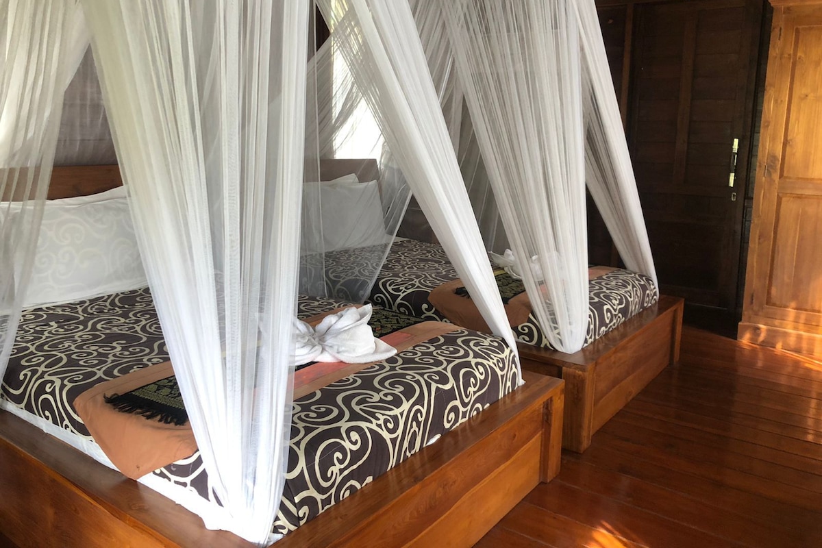A four-poster canopy bed with a patterned bedspread and pillows, wooden headboard, and a wooden floor.