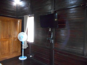 A room with a wooden door, a standing fan, and a television mounted on the wall. - Cozzy Kubu Alas Tunggal Villa (Karangasem)
