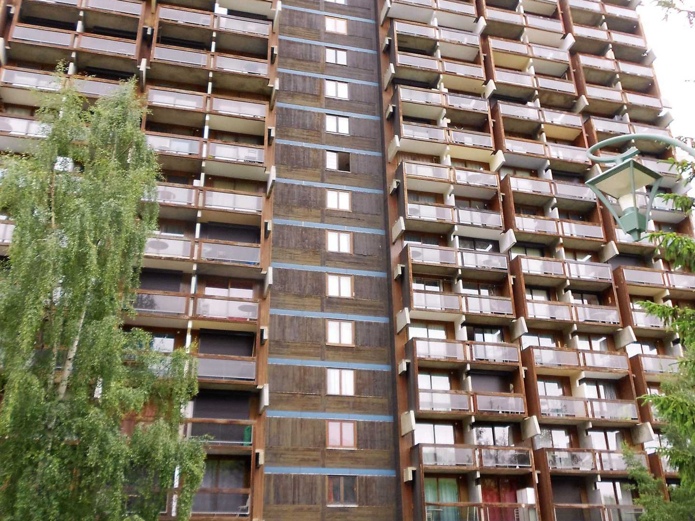 A multi-story residential building with balconies, wooden paneling, and a central stairwell.