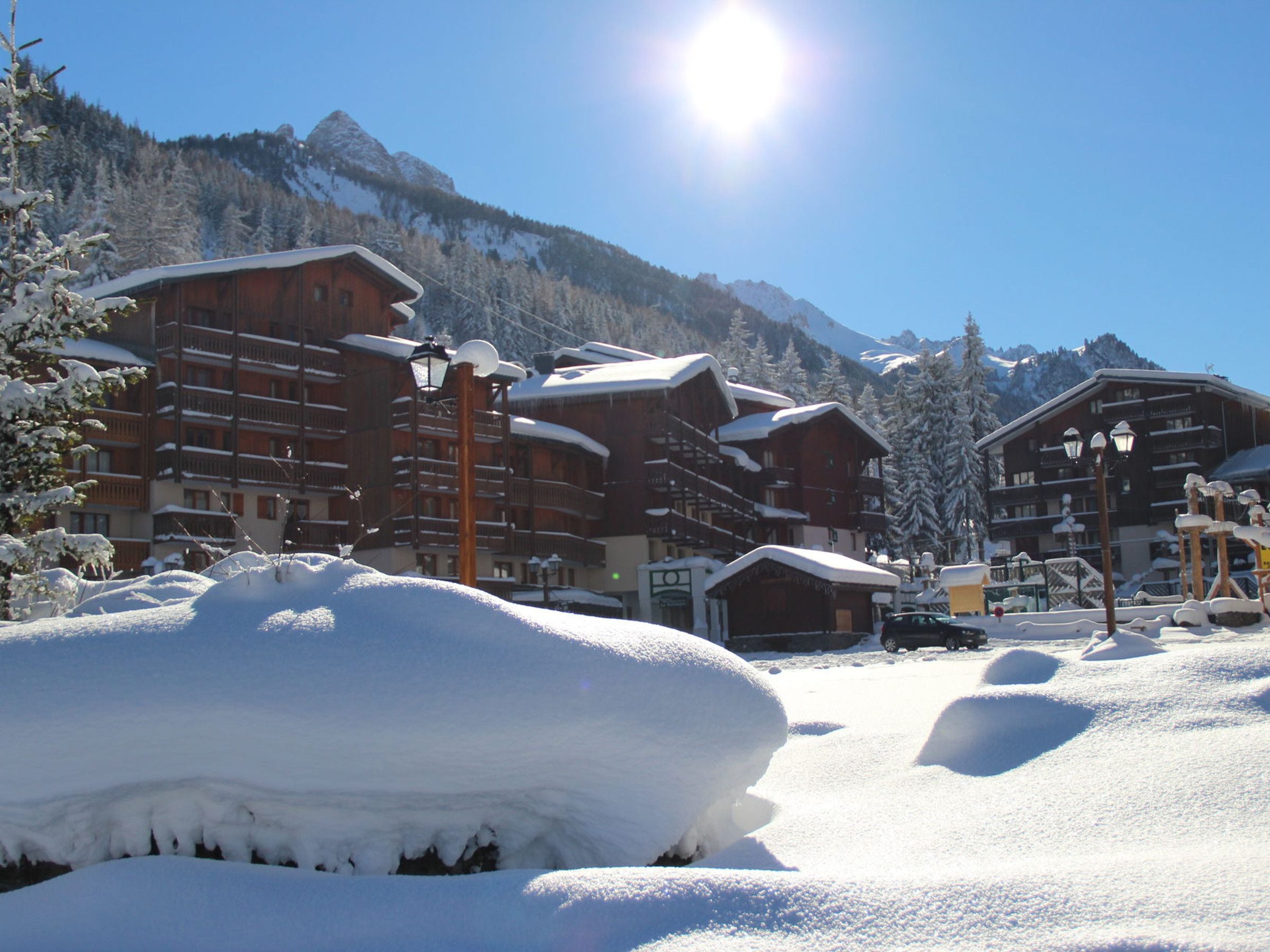 A snow-covered mountain resort with wooden buildings, a clear sky, and a bright sun.