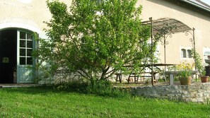 Un edificio con pared de piedra, un árbol y una pérgola metálica.