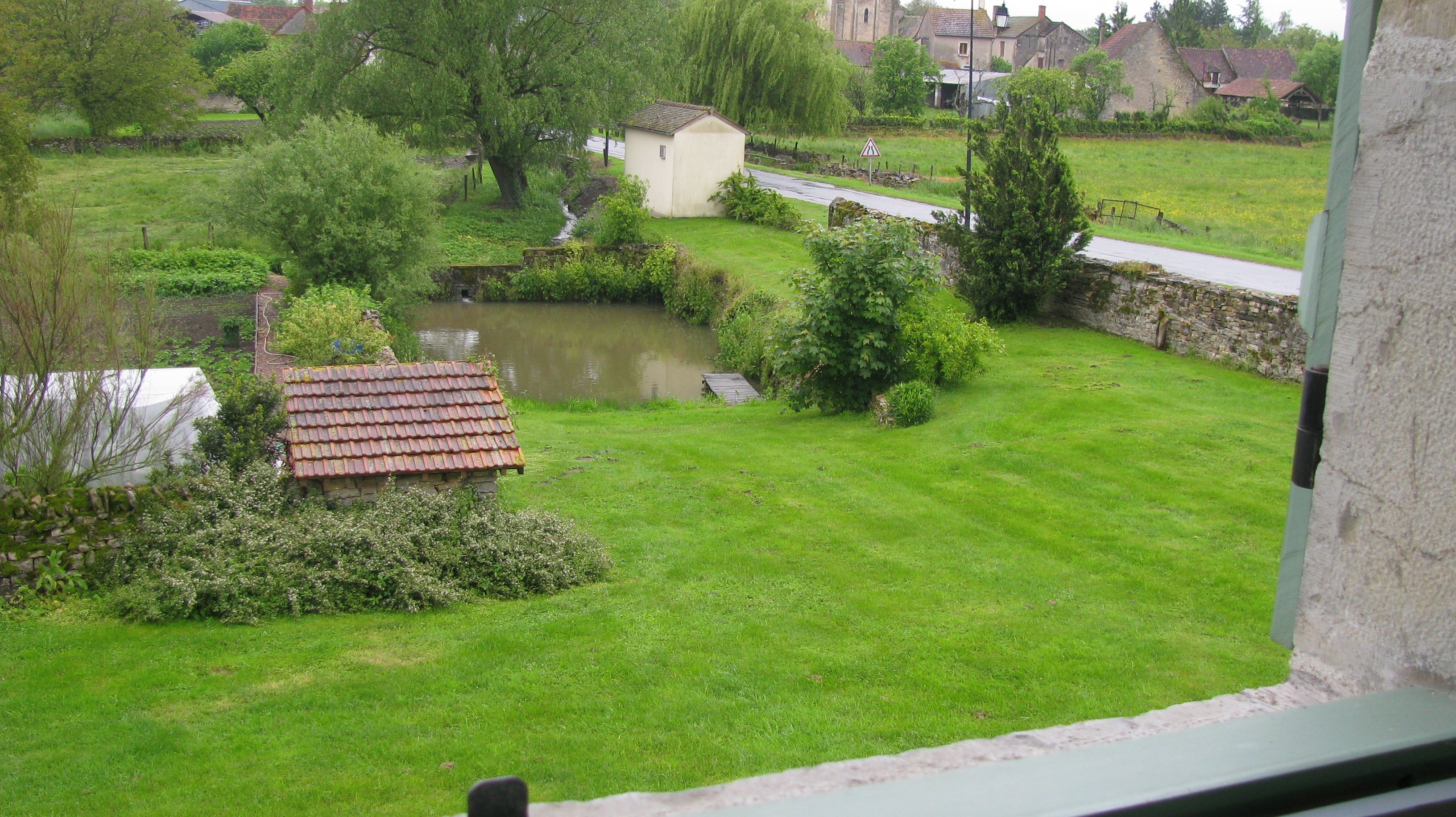 Een landelijk landschap met een klein vijvertje, een gazon en een gebouw met een pannendak.