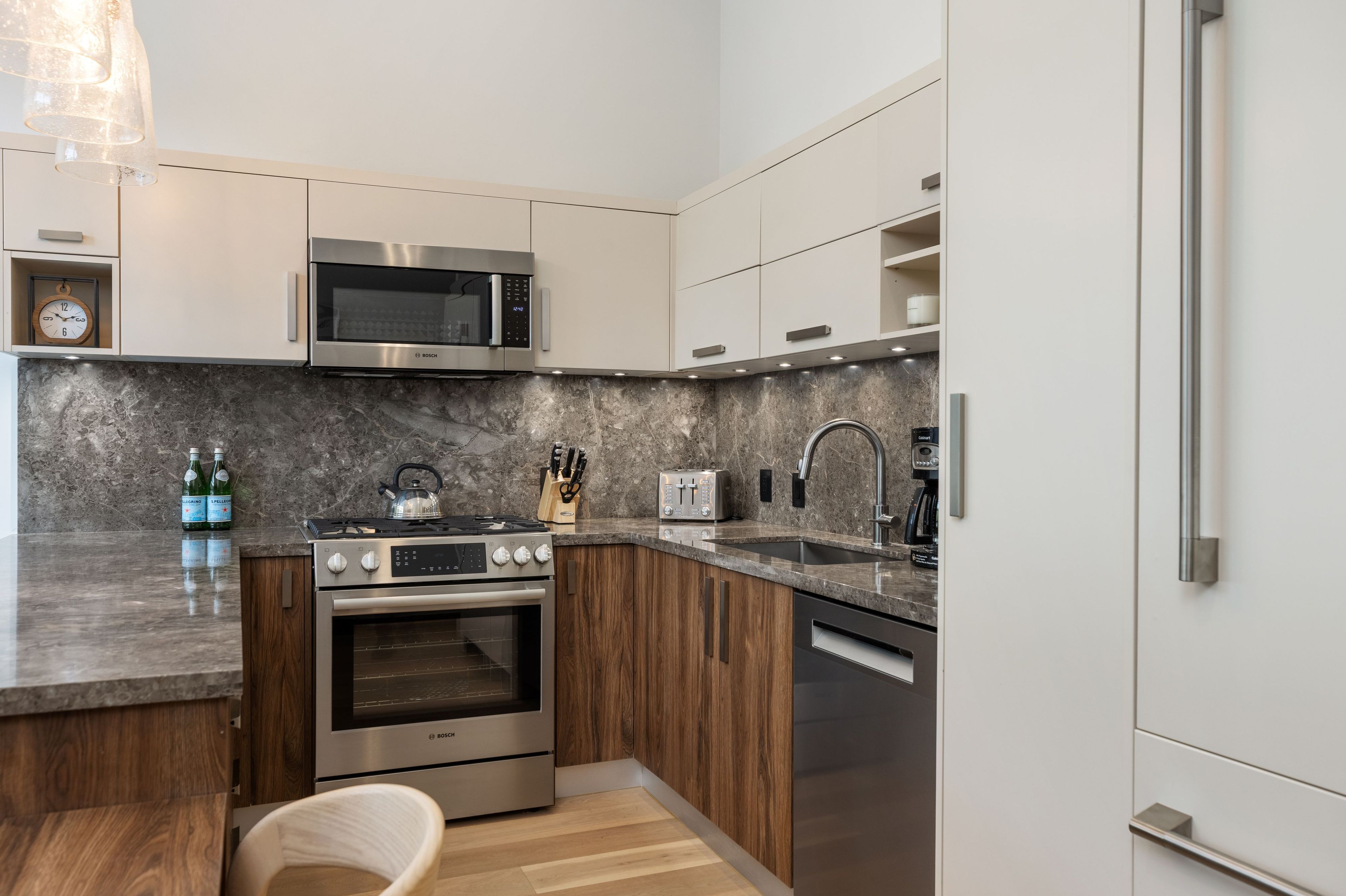 A modern kitchen with a Bosch oven, microwave, and dishwasher, a wooden cabinet, and a marble countertop.