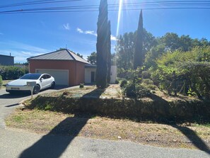 Un quartier résidentiel avec une voiture blanche garée devant une maison, un garage et un jardin entouré d’une clôture.