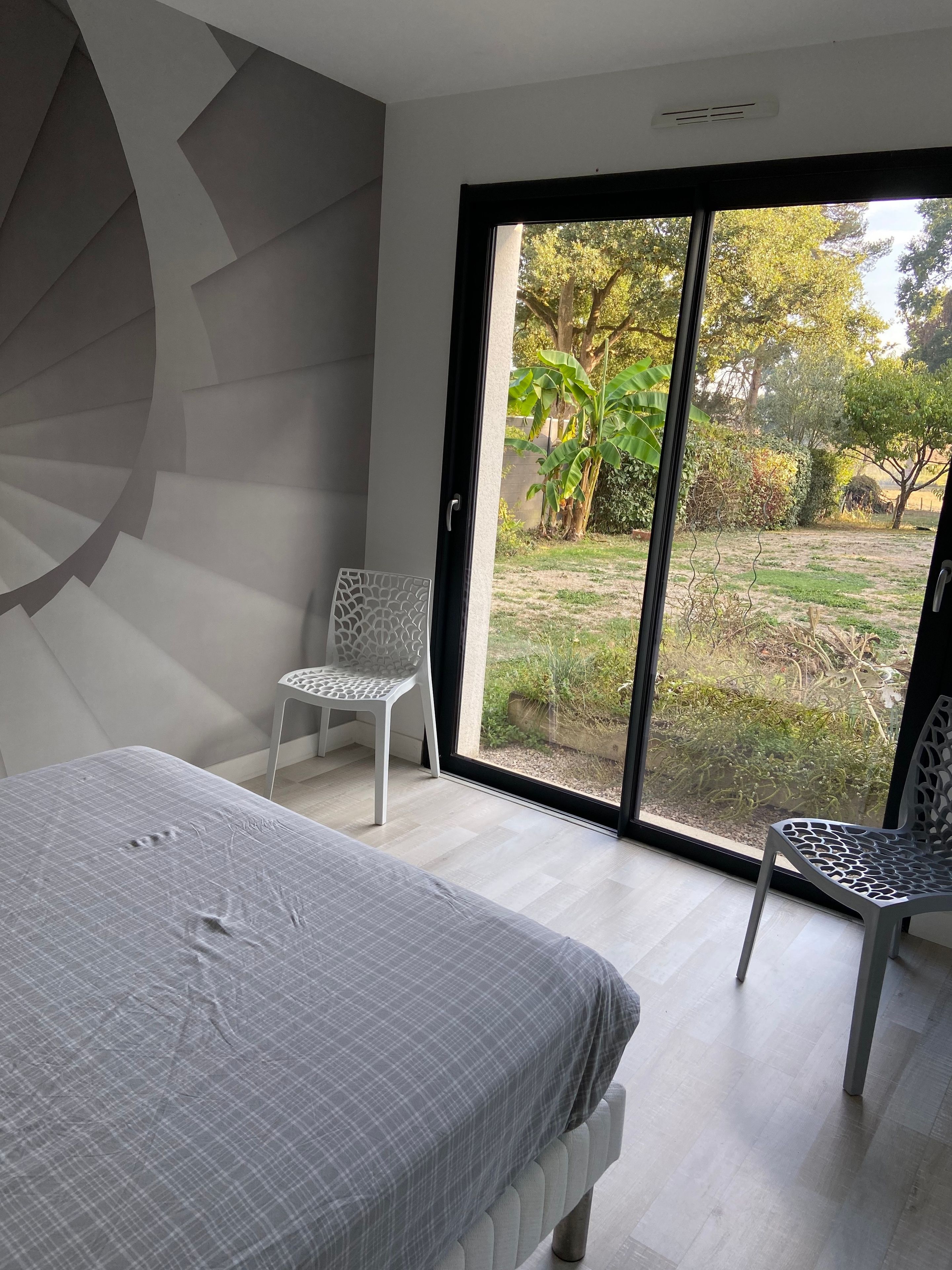Een slaapkamer met een bed, een stoel en uitzicht op een tuin door een schuifdeur.