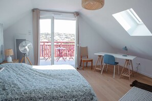 Une chambre avec un lit, un bureau, une chaise, un ventilateur et un balcon avec vue.