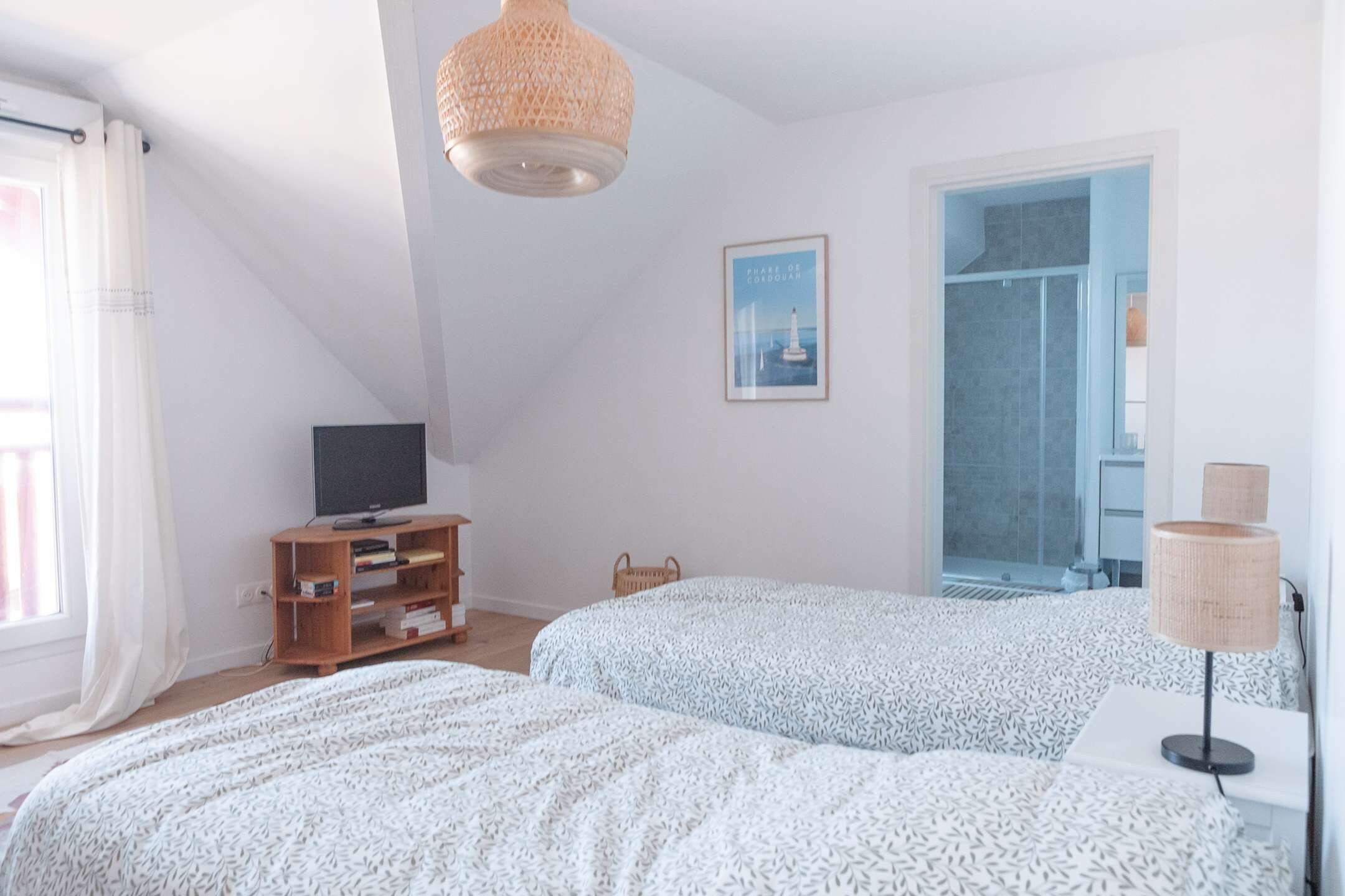 Une chambre avec deux lits, un téléviseur posé sur un meuble en bois, un tableau encadré au mur et une fenêtre avec des rideaux.