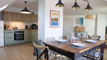 Une cuisine moderne avec des meubles en bois, un coin repas doté d’une table en bois pour quatre personnes, et un tableau encadré accroché au mur.