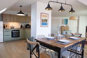 Une cuisine moderne avec des meubles en bois, un coin repas doté d’une table en bois pour quatre personnes, et un tableau encadré accroché au mur.