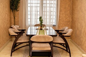 A dining area with a rectangular table, six chairs, a vase with a plant, and a window with sheer curtains. - Spacious unique 3 bedroom apartment (Lagos)