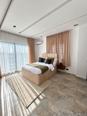 A modern bedroom with a large bed, a bedside table with a lamp, and an air conditioning unit. - Spacious unique 3 bedroom apartment (Lagos)