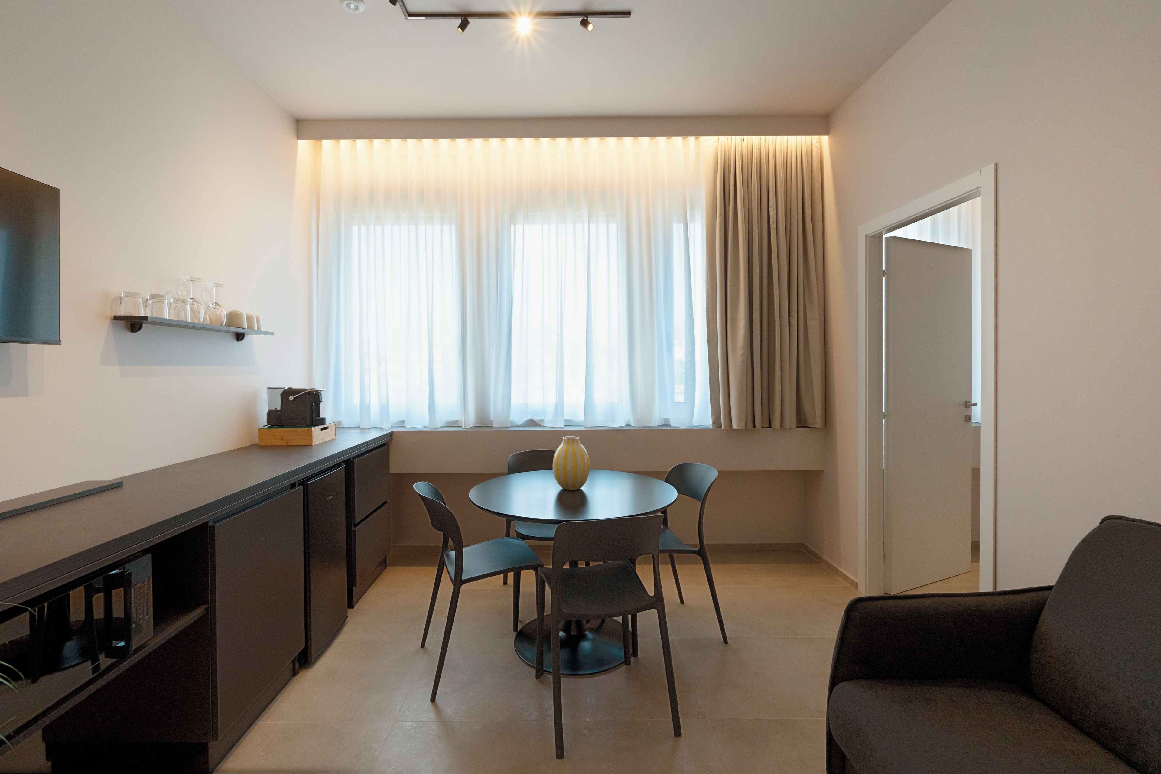 A compact living space with a kitchenette, a dining table with chairs, a sofa, and a window with curtains.