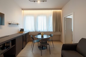 Un espacio habitable compacto con kitchenette, una mesa de comedor con sillas, un sofá y una ventana con cortinas.