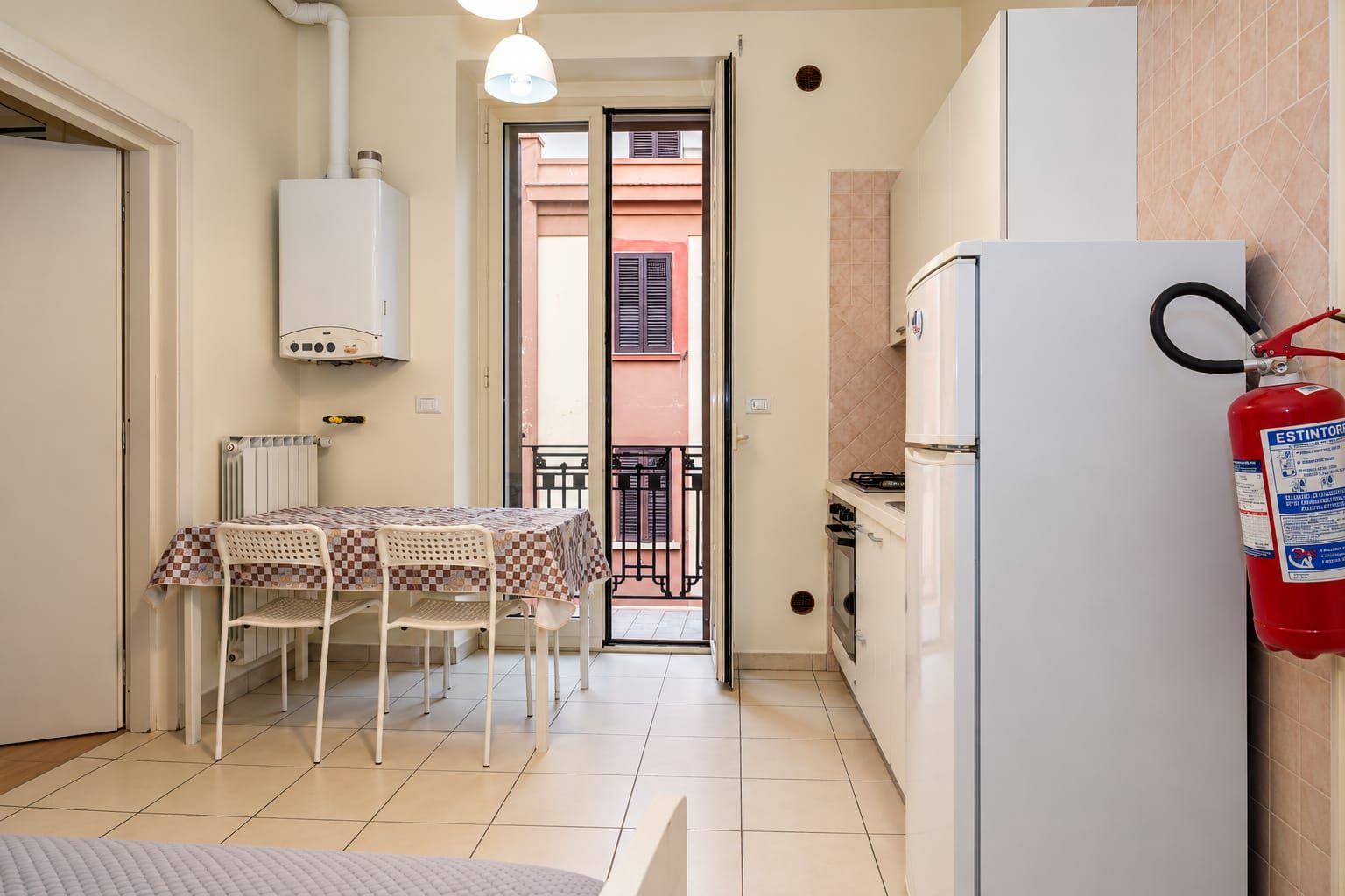 A compact kitchen with a dining area, a white refrigerator, a gas stove, and a fire extinguisher.