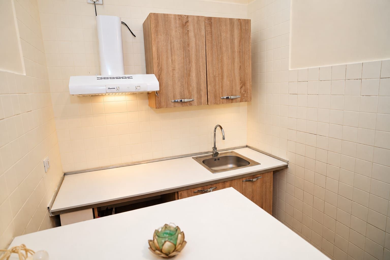 A compact kitchen with a white countertop, a stainless steel sink, and wooden cabinets.