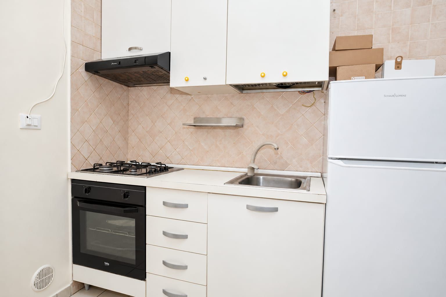 A kitchen with white cabinets, a gas stove, a built-in oven, a stainless steel sink, and a white refrigerator.