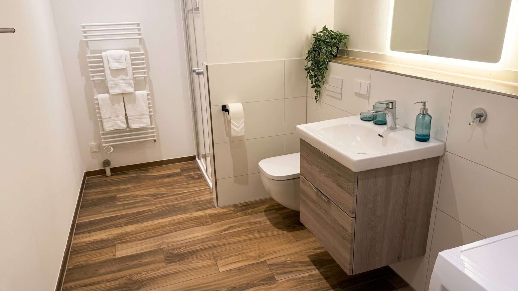 Ein modernes Badezimmer mit Holzboden, einem weißen Waschbecken mit Spiegel darüber und einer Toilette.