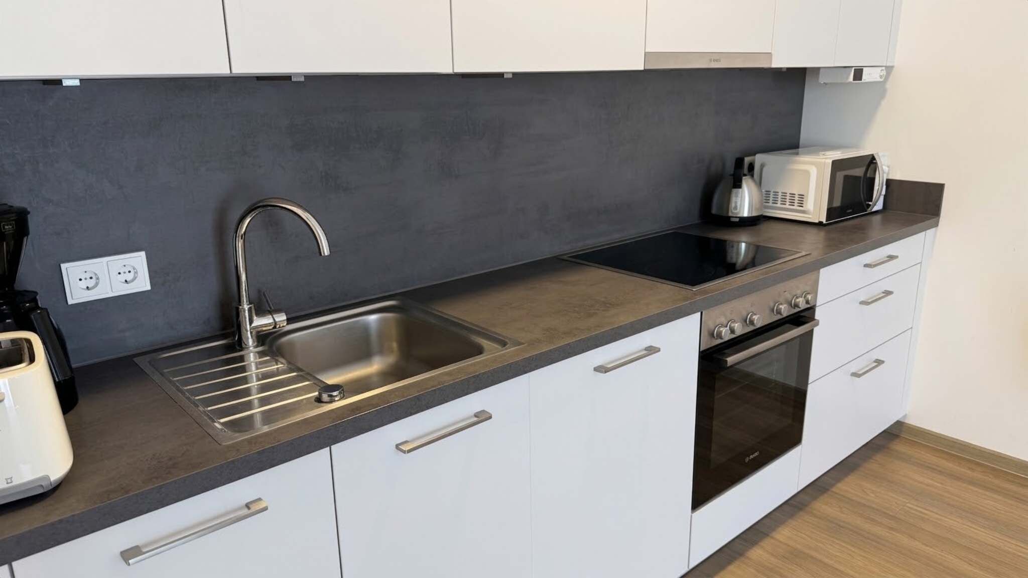 Eine moderne Küche mit einer Edelstahlspüle, einem eingebauten Backofen und einer Mikrowelle.