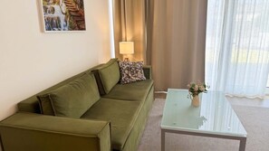 Ein Zimmer mit einem grünen Sofa, einem Glastisch, einer Lampe und einem Bild an der Wand.