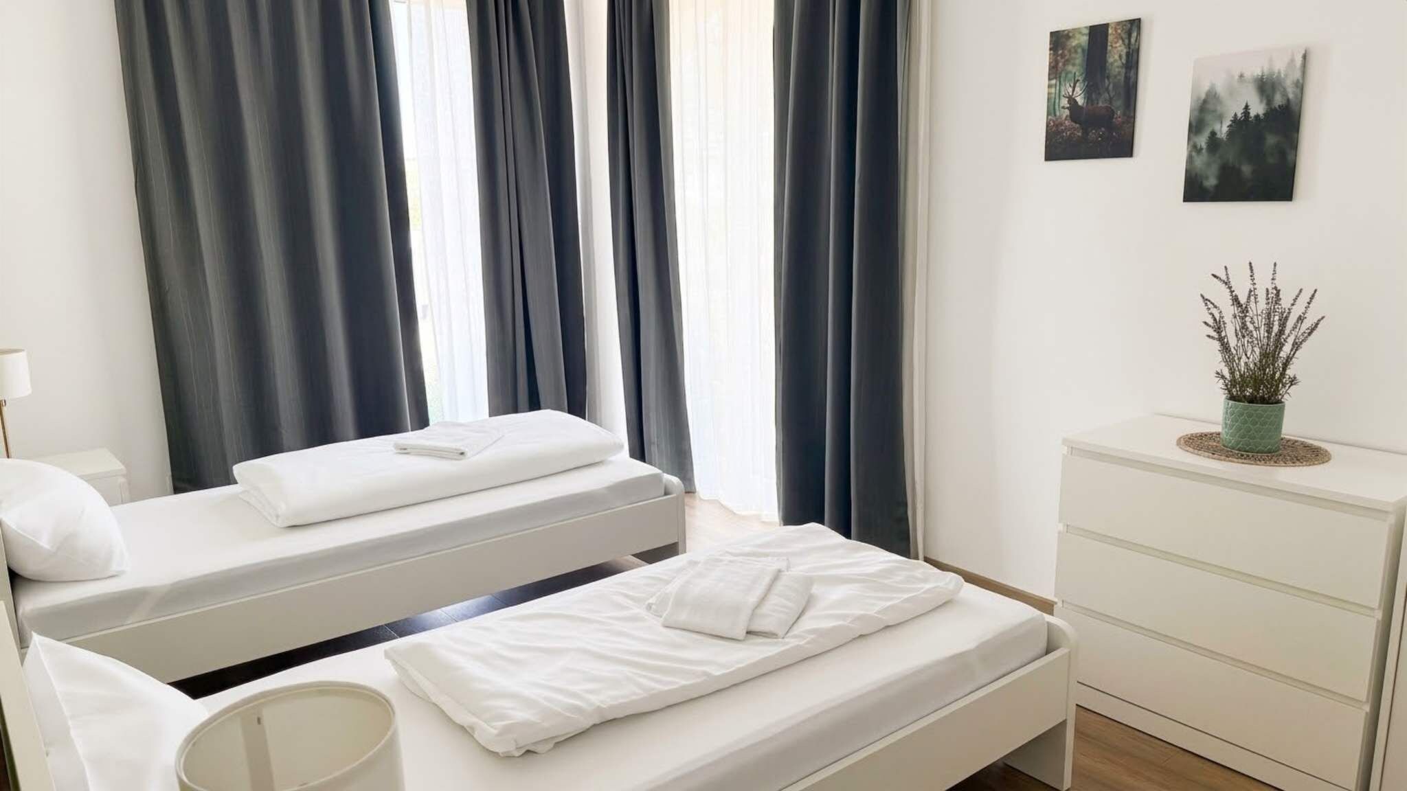 Ein Hotelzimmer mit zwei Betten, einem Nachttisch, einer Kommode und einem Fenster mit Vorhängen.