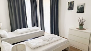 Ein Hotelzimmer mit zwei Betten, einem Nachttisch, einer Kommode und einem Fenster mit Vorhängen.
