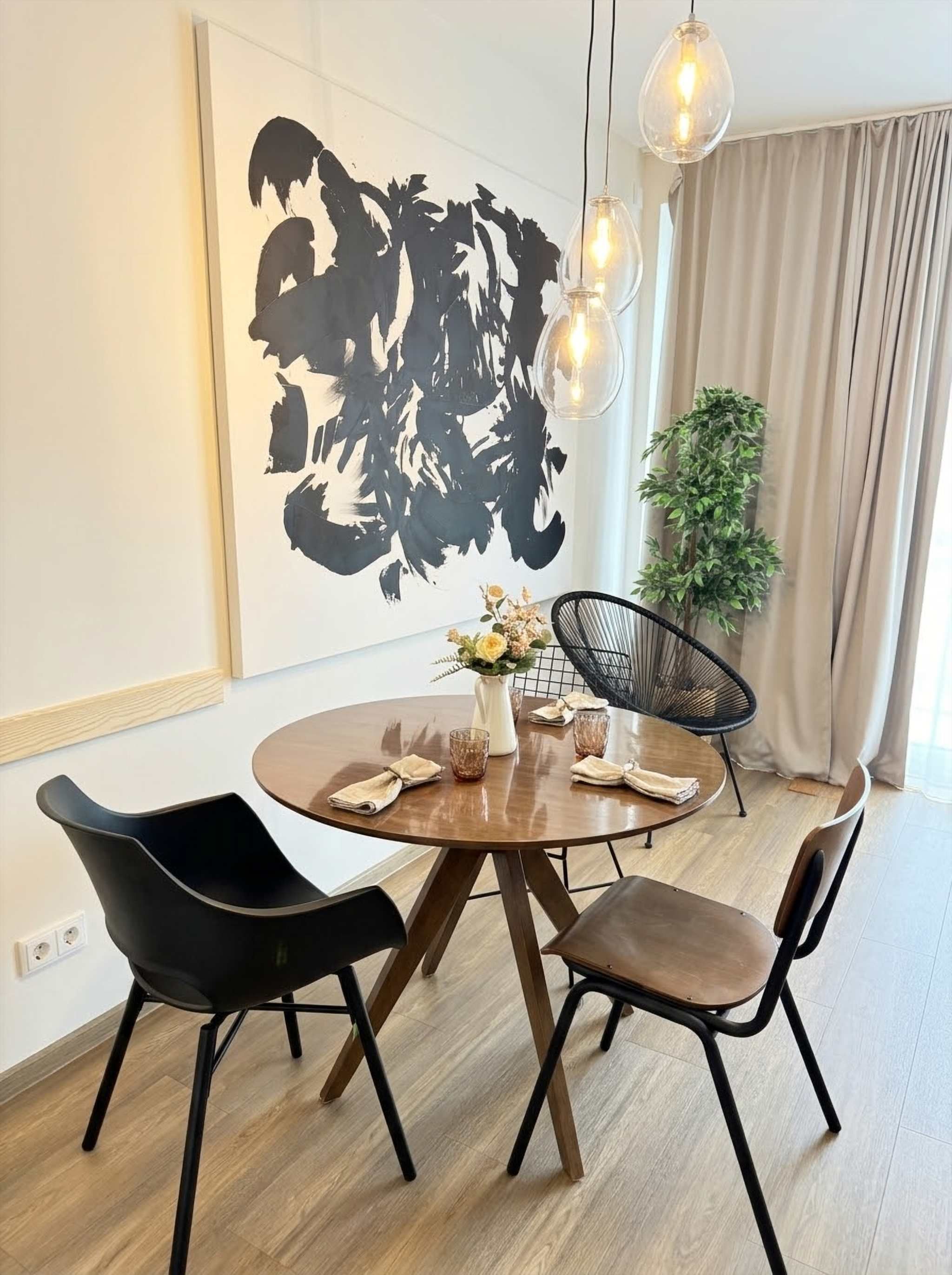 Ein Essbereich mit einem runden Tisch, vier Stühlen, einer Blumenvase und einem großen, abstrakten Gemälde an der Wand.