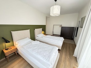 Ein Hotelzimmer mit zwei Betten, einem Nachttisch mit Lampe, einer Hängelampe und einem Kleiderschrank.
