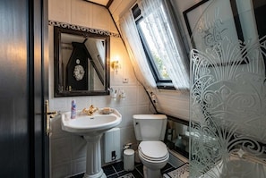 Ein Badezimmer mit Waschtisch, Toilette, einem Spiegel mit dekorativem Rahmen und einem Fenster mit Vorhängen.