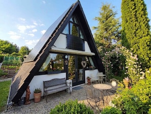 Ein modernes Haus mit geneigtem Dach, großen Fenstern und einer Terrasse mit Gartenmöbeln.