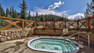 A hot tub with a stone wall and wooden railing, surrounded by a forest.
