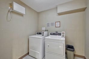 A laundry room with two stacked washers and dryers, a trash can, and a wall-mounted electrical outlet. - Fireside #202 | 3 Peaks Rentals (Sun Peaks)