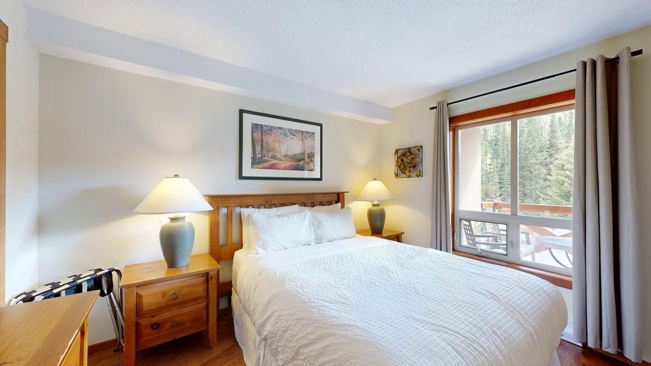A hotel room with a large bed, two bedside tables with lamps, a painting on the wall, and a window with curtains.