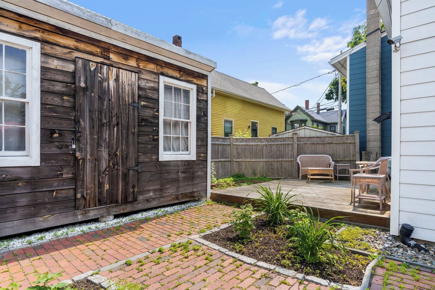 Une maison en bois avec un jardin clôturé, une terrasse dotée de mobilier d’extérieur et un espace jardin.