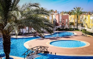 A pool area with multiple swimming pools, palm trees, and a building complex in the background.