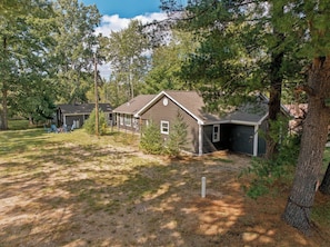 A residential area with houses surrounded by trees, a clear sky, and a dirt path. - Lakefront Retreat | Sandy Beach, Private Dock, Kayaks, Fire Pit & Arcade Games (Gladwin)