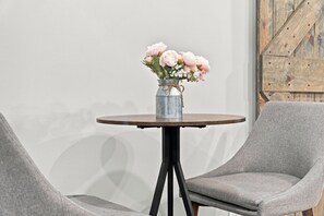 A round table with a metal vase containing flowers, flanked by two grey upholstered chairs. - Lakefront Retreat | Sandy Beach, Private Dock, Kayaks, Fire Pit & Arcade Games (Gladwin)