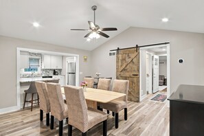 A modern kitchen with a dining area, a ceiling fan, and a sliding barn-style door. - Lakefront Retreat | Sandy Beach, Private Dock, Kayaks, Fire Pit & Arcade Games (Gladwin)