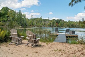 Two Adirondack chairs facing a lake with a dock extending into the water.