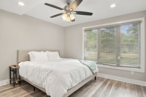 A bedroom with a bed, a ceiling fan, a window with blinds, and a nightstand. - Lakefront Retreat | Sandy Beach, Private Dock, Kayaks, Fire Pit & Arcade Games (Gladwin)