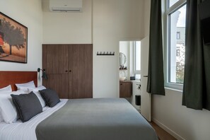 Habitación de hotel con cama, armario, baño visible a través de una puerta abierta y ventana con cortinas.