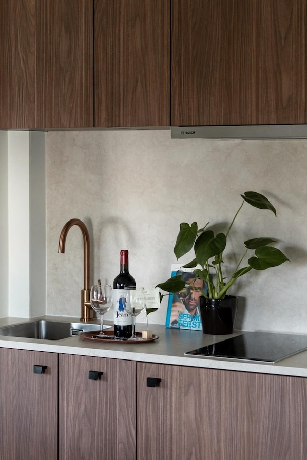 Una cocina con un armario de madera, un lavamanos de acero inoxidable, una botella de vino, dos copas de vino y una planta en maceta.