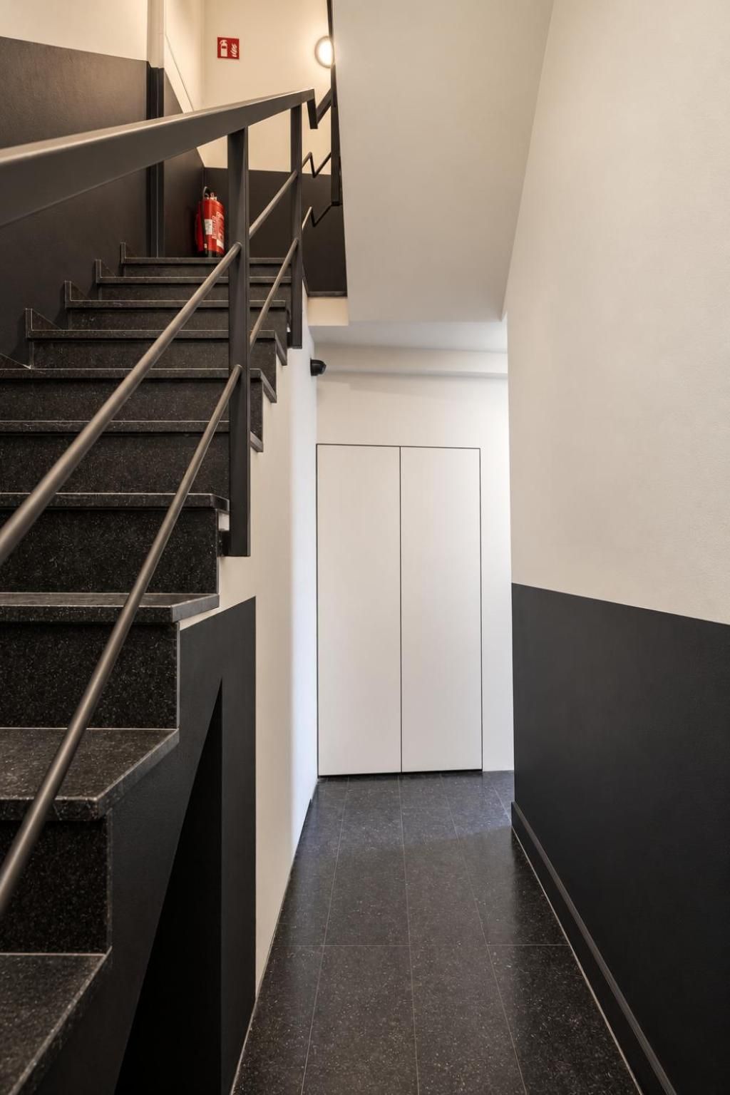 Een moderne trap met een metalen leuning en zwarte treden die naar een witte deur leiden.