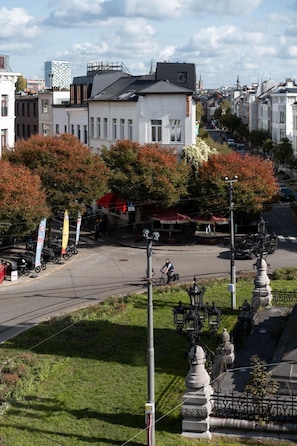 A street view with a row of trees in autumn colors, a white building with a dark roof, and a clear sky. - A Place - Marnixplaats 15 (Antwerpen)