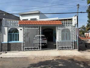 Una entrada con portón a una propiedad de fachada blanca, techo de tejas y un vehículo estacionado dentro.