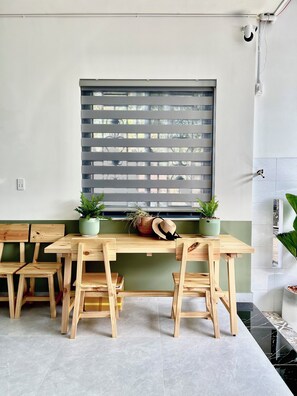 Un comedor con mesa y sillas de madera, una ventana con persianas y plantas en macetas.