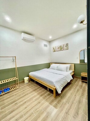 Un dormitorio con una cama de madera, aire acondicionado instalado en la pared, una mesita de noche pequeña y un estante en la pared.